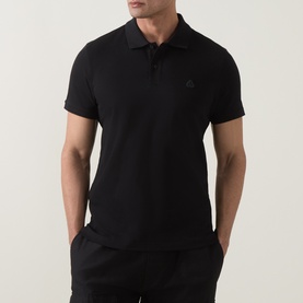 Model wearing Moose Knuckles black cotton polo shirt with tonal chest logo, styled with black trousers.