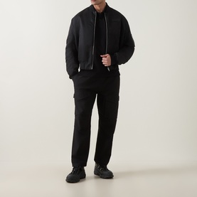 Model wearing Moose Knuckles Black Polo with black bomber jacket, cargo trousers, and black trainers.