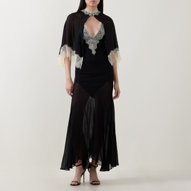 Model wearing Munthe Cielo Cape Dress in black with detachable sheer cape, silver lace trim at neckline, and midi-length slip silhouette