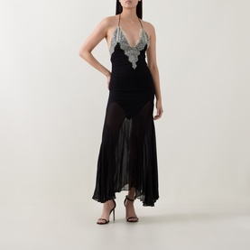 Model wearing Munthe Cielo Cape Dress in black with silver lace trim bodice, V-neckline, slim straps, and sheer midi skirt, styled with black heeled