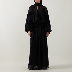 Model wearing Munthe Solana Pussy-Bow Gown Dress in black with puff sleeves, gathered waist, and pleated maxi skirt