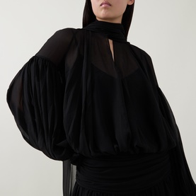 Model wearing Munthe Solana Pussy-Bow Gown Dress in black with sheer puff sleeves, pussy-bow collar, and gathered waist detail.