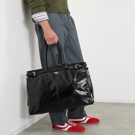 Model carrying Prada Bonnie Triangle Logo Holdall in black nylon and leather with glossy finish, top handles, buckle straps; styled with red trainers