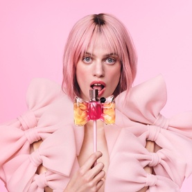 Viktor & Rolf Flowerbomb EDP held by model in pink bow top, pink background, floral bottle with red cap
