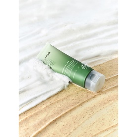 Anua cleanser in sage green tube, shown on sandy surface with white foamy texture swatched alongside