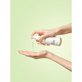 Anua cleanser pump bottle dispensing product into open palm, shown against a soft green background