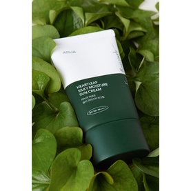 Anua Heartleaf Silky Moisture Sun Cream SPF tube in dark green and white packaging, surrounded by green leaves