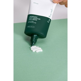 Anua Heartleaf Silky Moisture Sun Cream SPF in green tube, dispensing white cream onto green surface