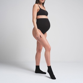 Model wearing Skims black bralette, styled with matching black maternity briefs and ankle socks
