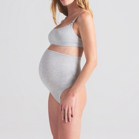 Model wearing Skims light heather grey bralette, styled with matching high-waist briefs, shown on a pregnancy bump.