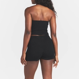 Model wearing Skims black strapless bandeau top, shown from behind, styled with matching black shorts.