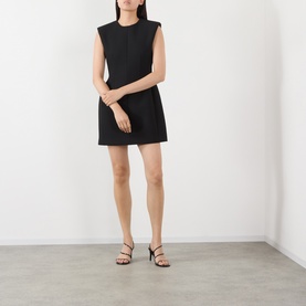 Model wearing The Frankie Shop black sleeveless mini dress with padded shoulders, styled with black strappy heeled sandals.