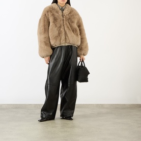 Model wearing The Frankie Shop Light Taupe faux fur bomber jacket, styled with black wide-leg leather trousers and a small black tote bag.
