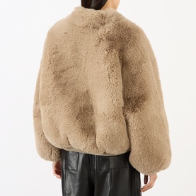 Model wearing The Frankie Shop light taupe faux fur jacket, back view, styled with black leather trousers
