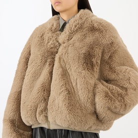 Model wearing The Frankie Shop light taupe faux fur bomber jacket, styled with black leather trousers and grey top.
