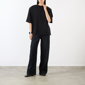 Model wearing The Frankie Shop black oversized cotton T-shirt, styled with wide-leg black trousers and black loafers.