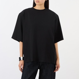Model wearing The Frankie Shop black oversized cotton T-shirt with drop shoulders, styled with dark denim jeans and a silver cuff bracelet.