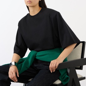Model wearing The Frankie Shop black cotton oversized T-shirt, seated, styled with green knotted layer and dark jeans.