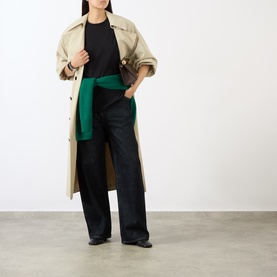 Model wearing The Frankie Shop black cotton T-shirt, styled with beige trench coat, green wrap detail, and wide-leg dark trousers.