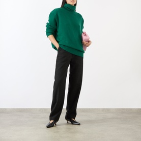 Model wearing The Frankie Shop Forest Green alpaca-blend turtleneck sweater with black straight-leg trousers, styled with a pink clutch bag.