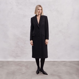Model wearing The Landskein black longline tailored coat with notch lapels and patch pockets, styled with black tights and flat shoes