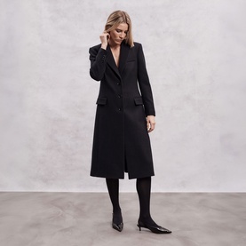 Model wearing The Landskein black longline coat, styled with black tights and kitten heel pumps