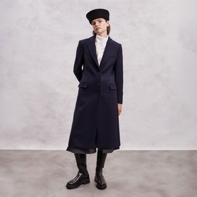 Model wearing The Landskein black tailored longline coat, styled with white shirt, wide-leg trousers, black cap and chunky boots.