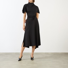 Model wearing Victoria Beckham black midi dress with high neck, flutter sleeves, wrap waist, and asymmetric hem, styled with black heels