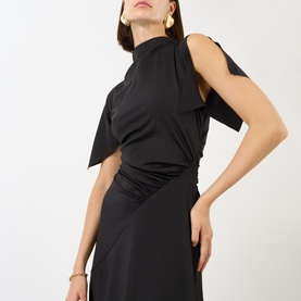 Model wearing Victoria Beckham black asymmetric one-shoulder dress with draped cape detail and ruched waist, styled with gold earrings.