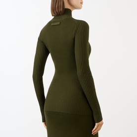 Model wearing Victoria Beckham Logo Rib-Knit Turtleneck Sweater in dark green, shown from back, with tonal logo badge and ribbed long sleeves.