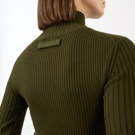 Model wearing Victoria Beckham Logo Rib-Knit Turtleneck Sweater in dark green, showing ribbed back detail and tonal logo badge at shoulder.