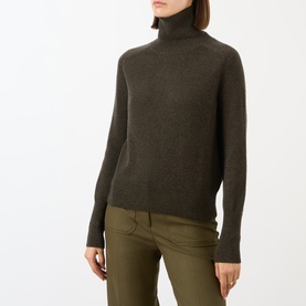 Model wearing Victoria Beckham Marie Turtleneck Sweater in dark green wool with ribbed trims, styled with olive trousers.