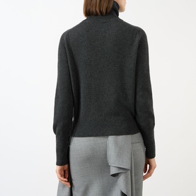 Model wearing Victoria Beckham Marie Turtleneck Sweater in dark grey wool, rear view, with ribbed trims, styled with grey wrap skirt.