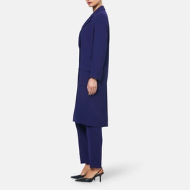 Model wearing Helen McAlinden Ink Blue longline coat with matching tailored trousers, styled with black pointed-toe heels, side profile view.
