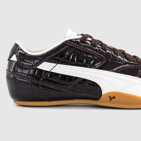 Dark brown croc-embossed patent leather Puma trainer with white stripe detail, brown laces, and gum sole, close-up angle