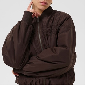 Model wearing Kaffe Arlette Cropped Bomber Jacket in Coffee Bean, showing draped smocked chest detail and zip fastening, close-up crop.