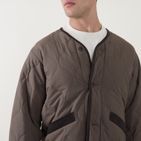 Model wearing Snow Peak dark brown quilted casual jacket with collarless neckline, snap button fastening, and contrast trim detail.
