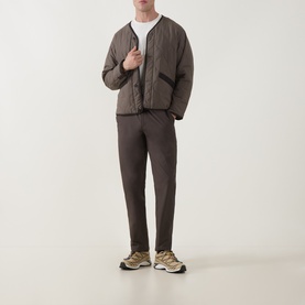 Model wearing Snow Peak dark brown quilted casual jacket, styled with matching trousers and cream T-shirt, with beige trainers.