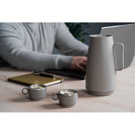 Tramontina beige mugs styled on a wooden desk alongside a matching vacuum jug, with a person working on a laptop in the background