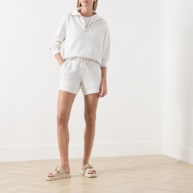 Model wearing Varley Ivory Marl shorts with matching half-zip sweatshirt and tan flatform sandals.