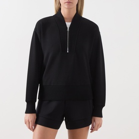 Model wearing Varley black half-zip sweat top with ribbed collar, styled with matching black shorts.