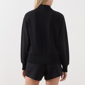 Model wearing Varley black sweat top, rear view, with matching black shorts. Relaxed fit with ribbed cuffs and hem.
