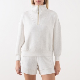 Model wearing Varley Ivory Marl half-zip sweatshirt with gold zip, styled with matching shorts.