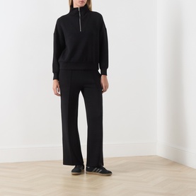 Model wearing Varley black half-zip sweat top with matching wide-leg trousers and black trainers.