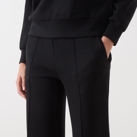 Model wearing Varley black wide-leg sweat trousers with front seam detail and side pockets, styled with a black sweatshirt.