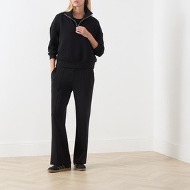 Model wearing Varley black quarter-zip sweatshirt styled with matching black wide-leg trousers and dark slider sandals.