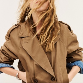 Model wearing Bash brown trench coat with epaulette detail, styled with denim shirt and delicate bracelet
