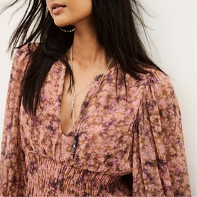 Model wearing Bash pink floral chiffon top with deep V-neck and elasticated waist, styled with layered silver necklaces.