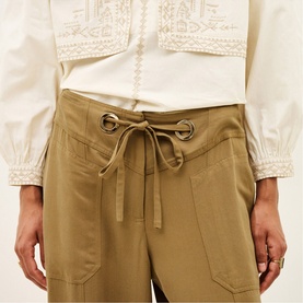 Model wearing Bash yellow wide-leg trousers with eyelet drawstring waist, styled with a white embroidered blouse.