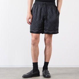 Model wearing Casablanca black silk shorts with tonal diamond and wave jacquard pattern, styled with black socks and loafers
